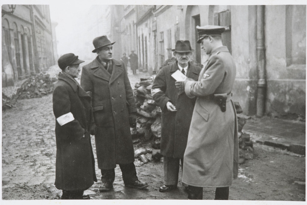 یک پلیس آلمانی مدارک شناسایی یهودیان در محله یهودی نشین کراکوف را بررسی می کند.  لهستان  در حدود 1941.
