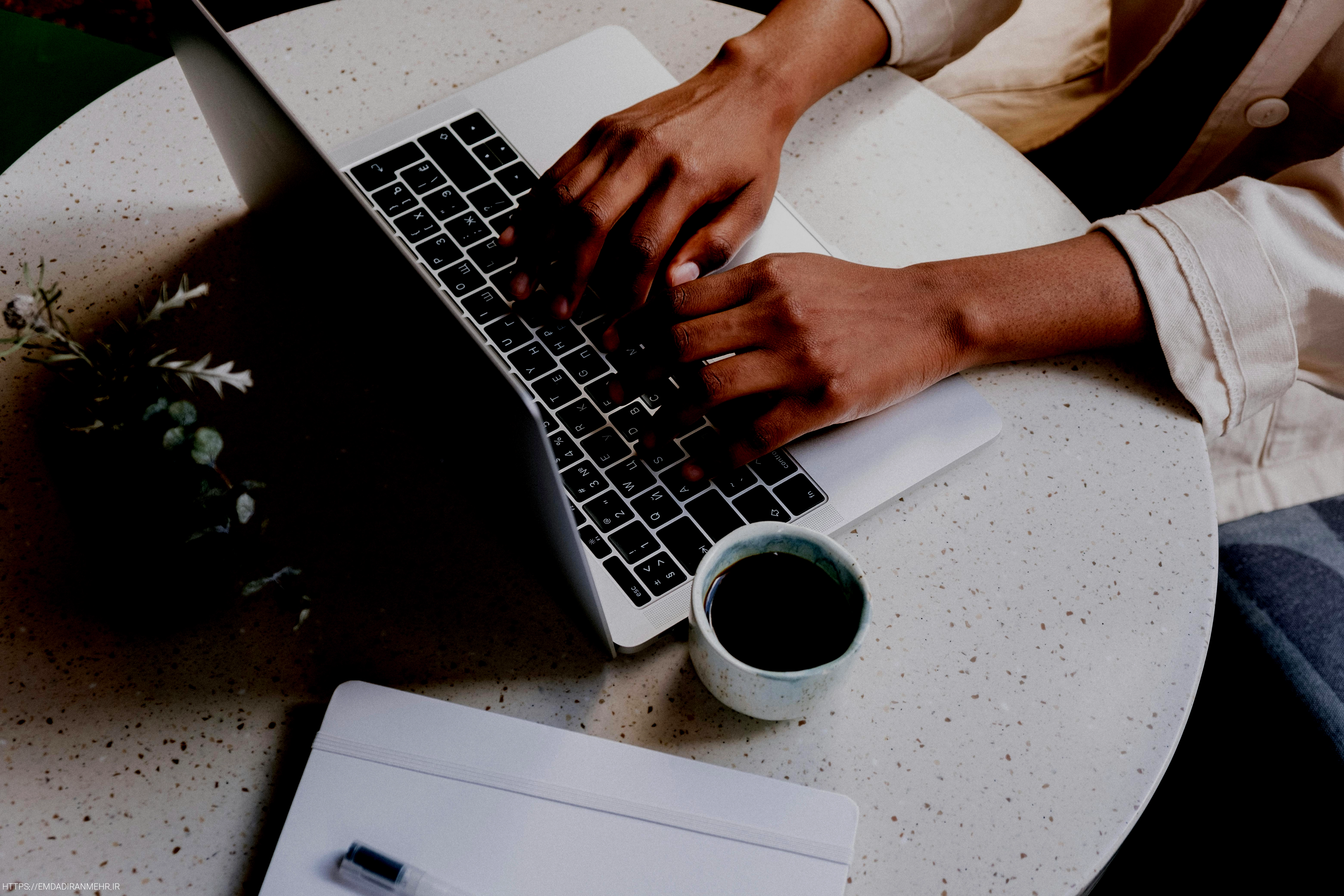 person using macbook pro beside white ceramic mug